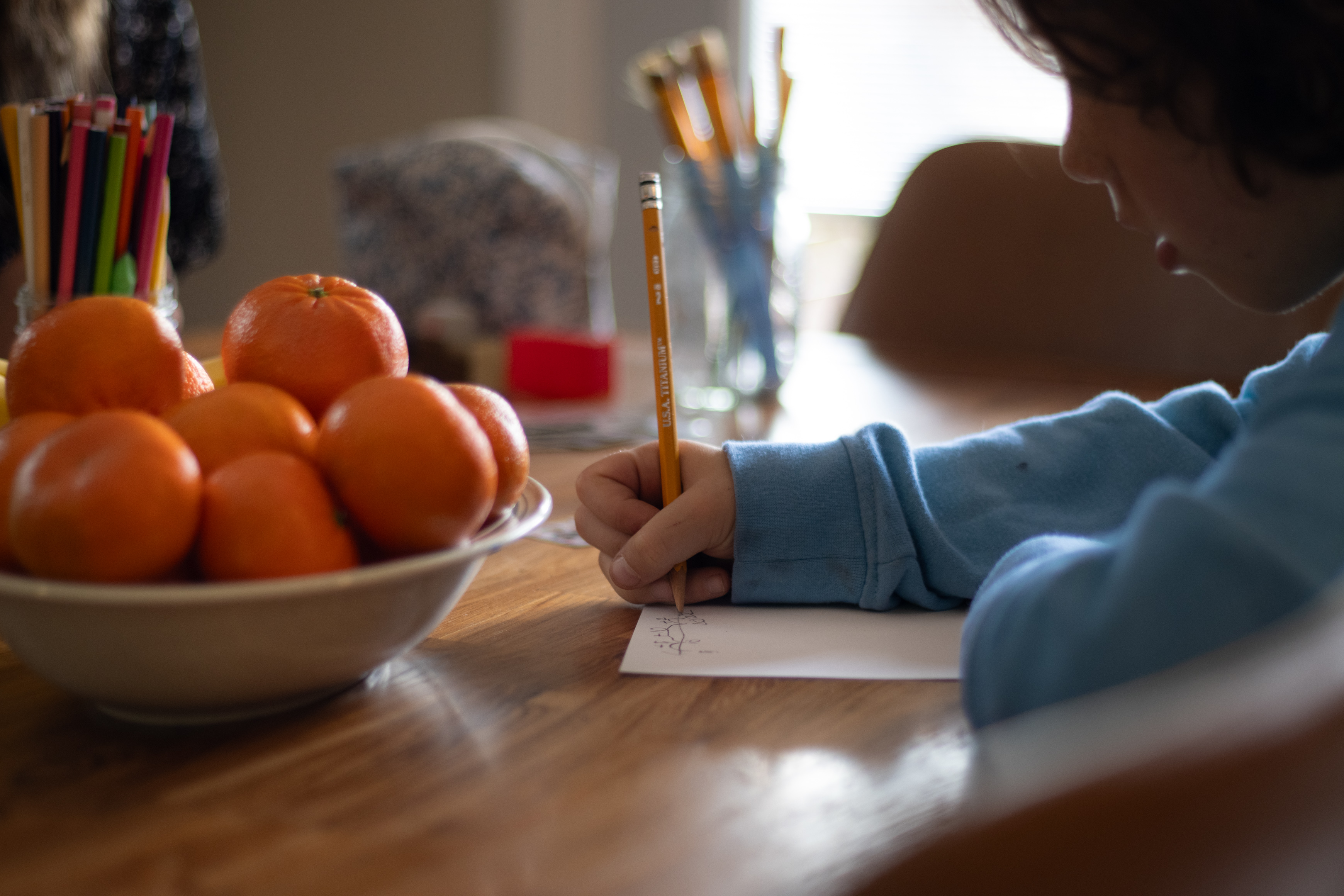 Student writing on paper beside a bowl of oranges